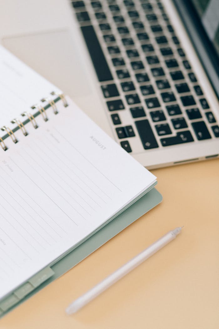 about-us-01 Open notebook next to a laptop and pen on a desk, ideal for business and planning.